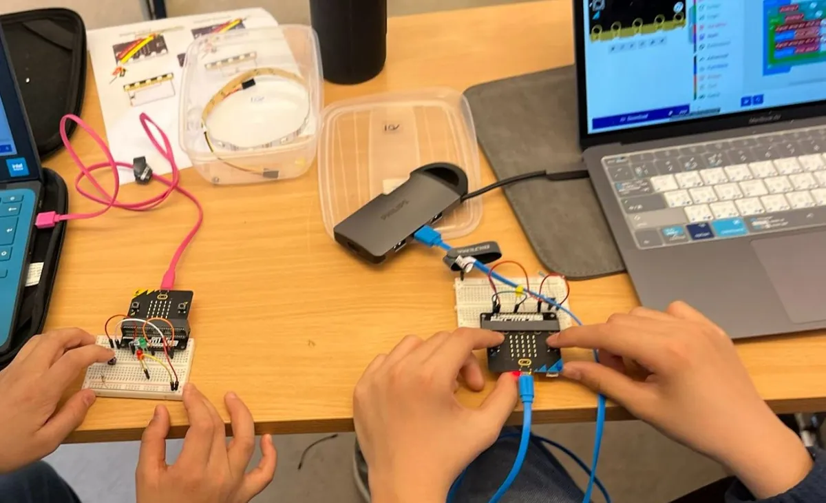 Hands working on two Micro:bit circuits on a table full of parts