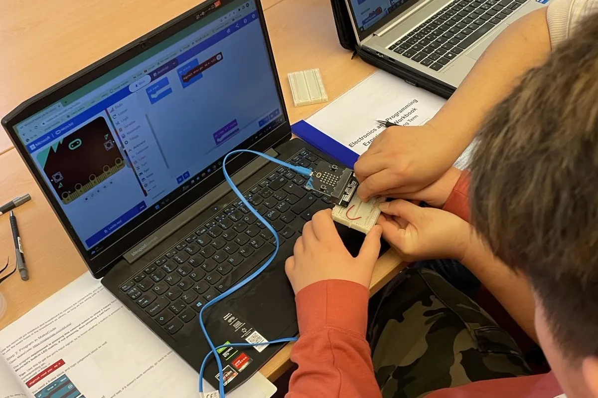 A student wires a breadboard next to the laptop with MakeCode open